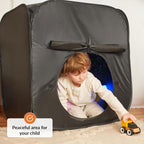 Child playing with a toy car inside a dark play tent with a starry light on a light wooden floor.