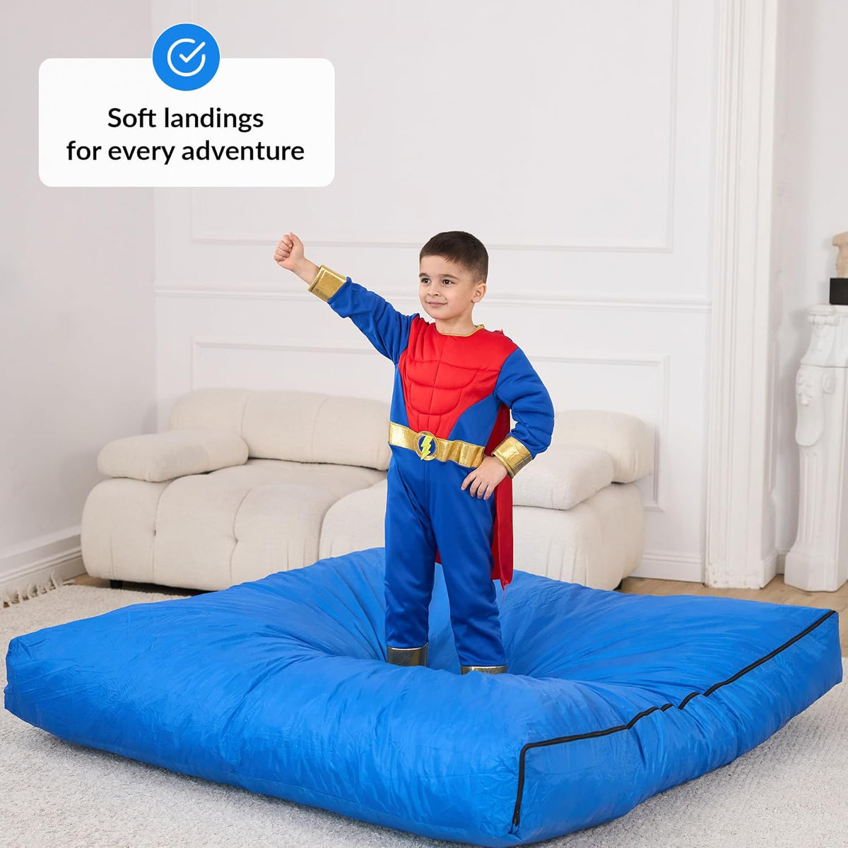 Child in superhero costume standing on a large blue mat with text 'Soft landings for every adventure' above.