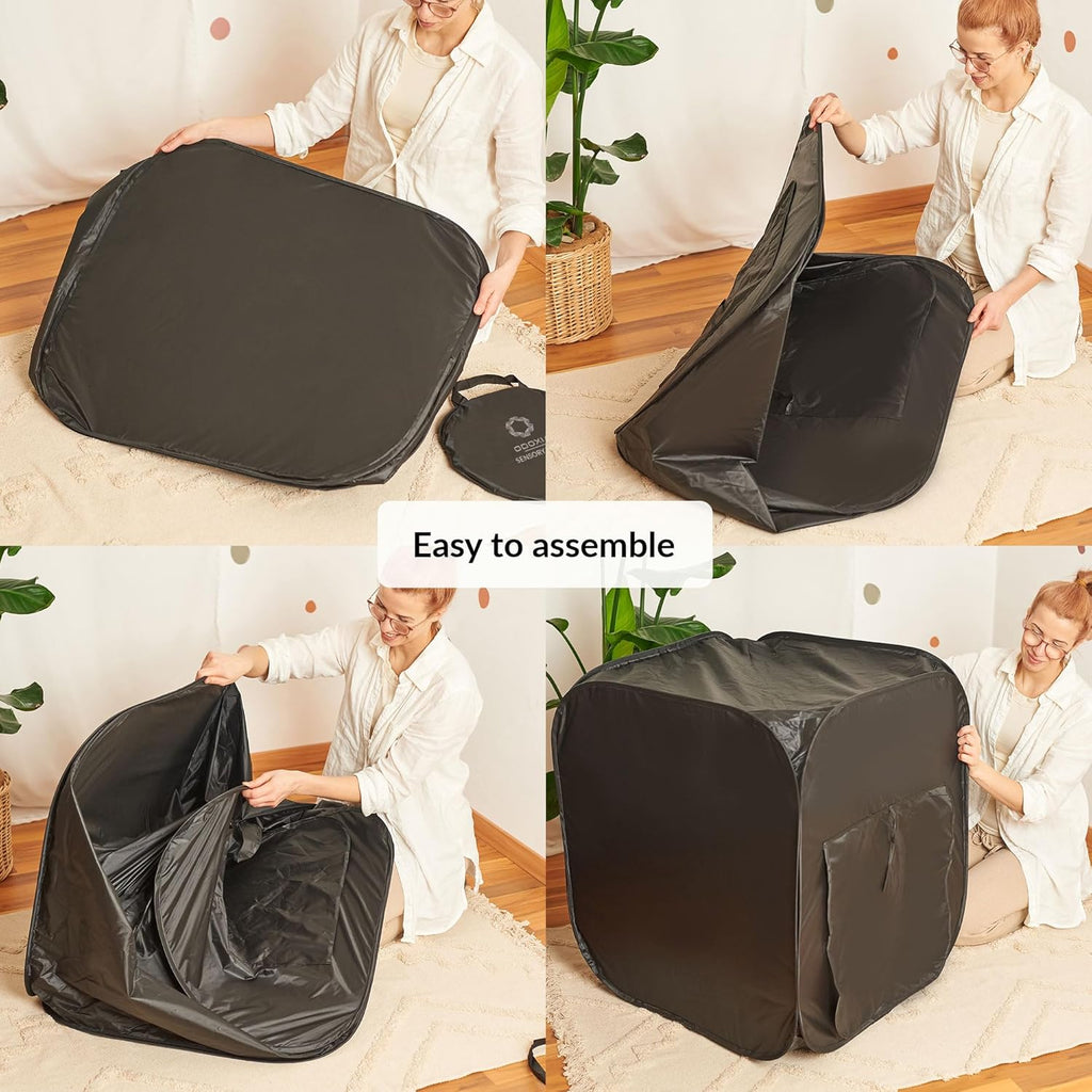 Person assembling a black pop-up tent in a room with plants and furniture.