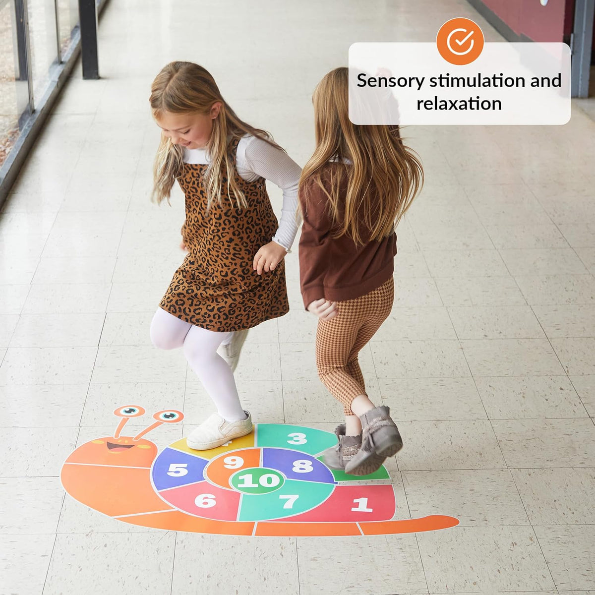 Two children playing on a colorful floor decal shaped like a snail with numbers.