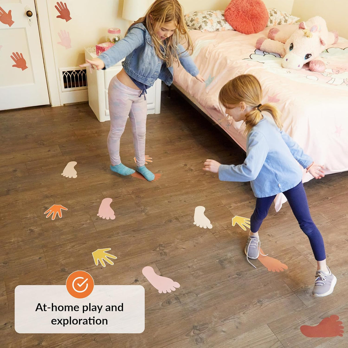 Two children playing with colorful hand and foot decals on a wooden floor.