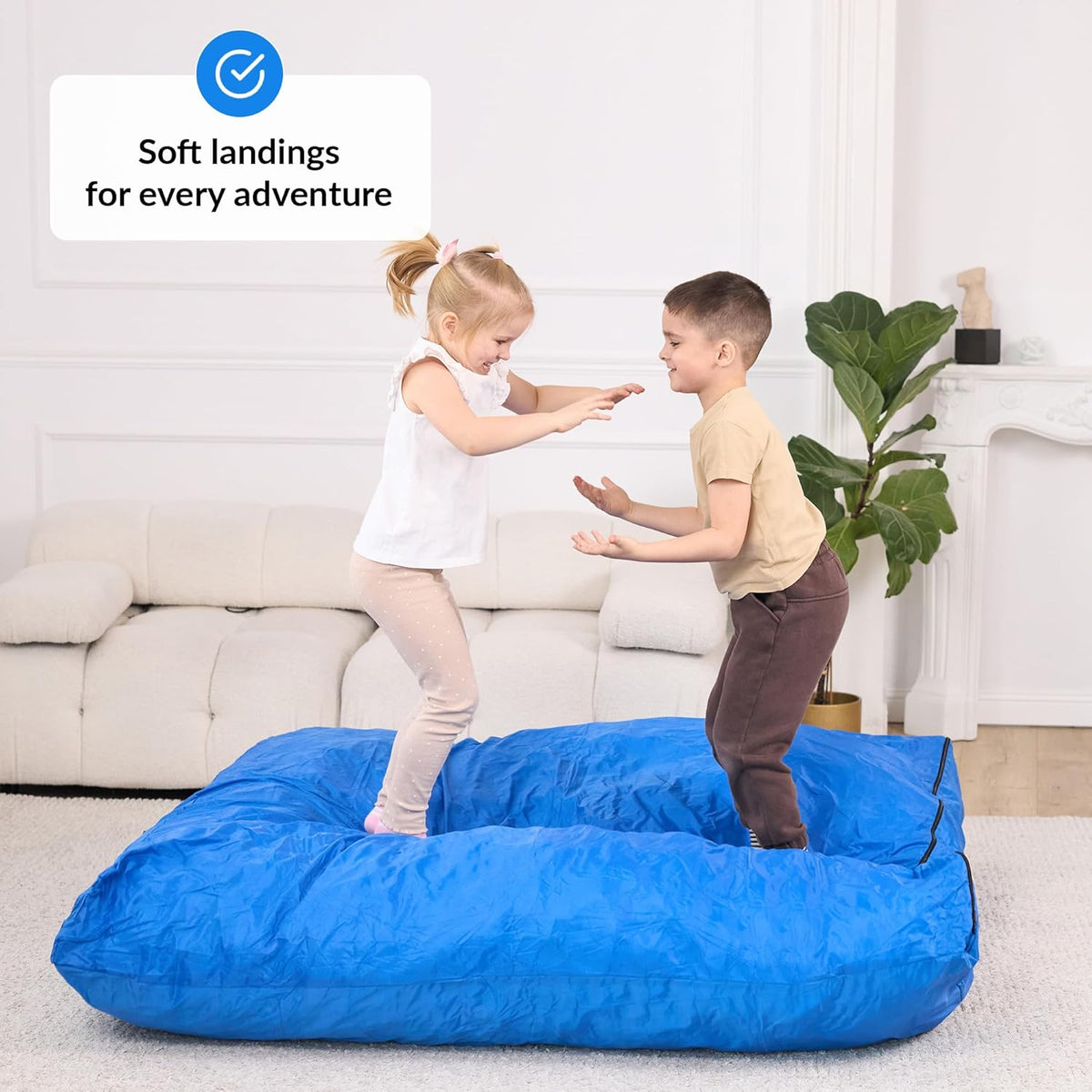 Two children playing on a large blue crash pad in a living room.