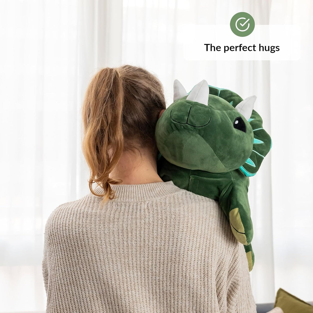 Person wearing a green dinosaur-shaped plush against a white curtain background