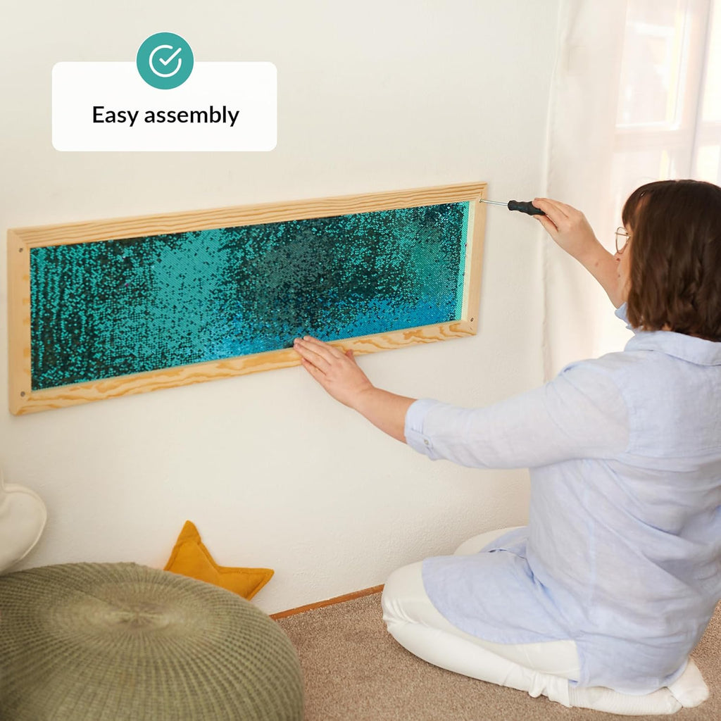 Person assembling a framed sequins wall with turquoise material on a wall.