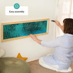 Person assembling a framed sequins wall with turquoise material on a wall.