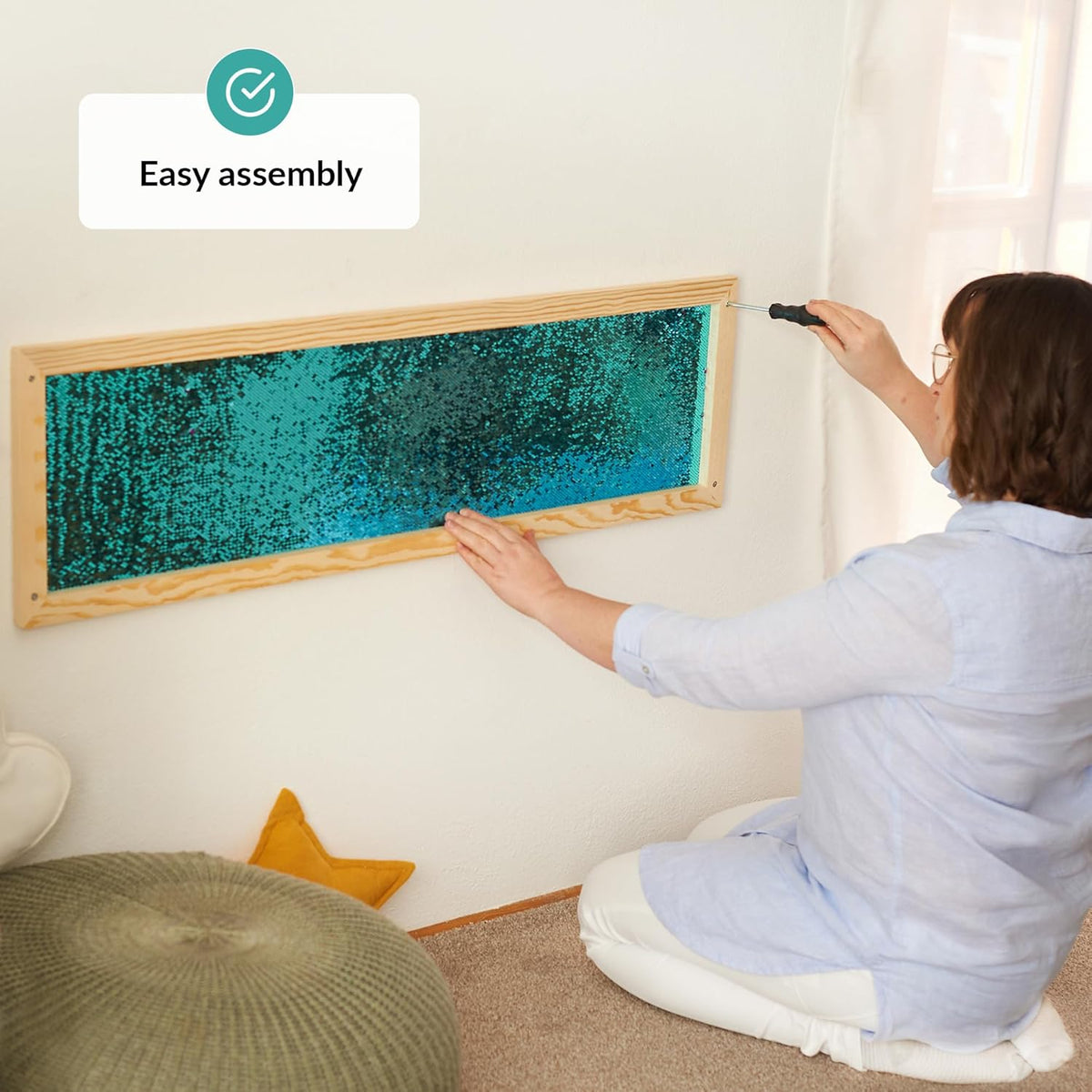 Person assembling a framed sequins wall with turquoise material on a wall.
