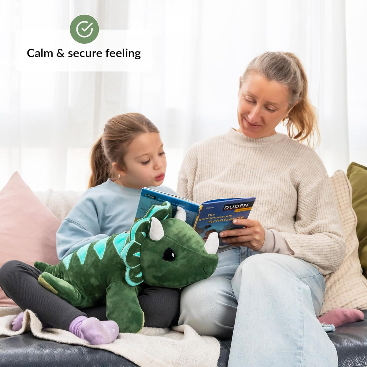 Woman and child reading a book together on a couch with a weighted dinosaur plush toy.