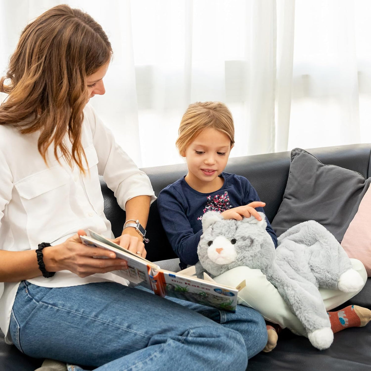 Woman reading a book to a child on a couch with a weighted lap cat