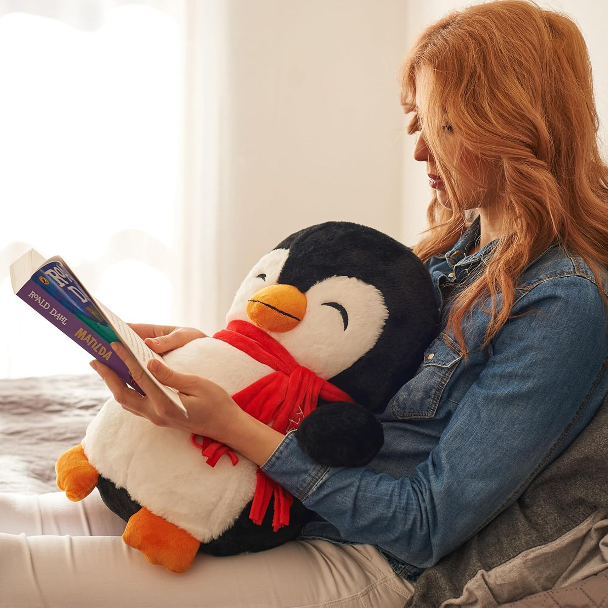 Woman reading a book to a large weighted plush penguin toy