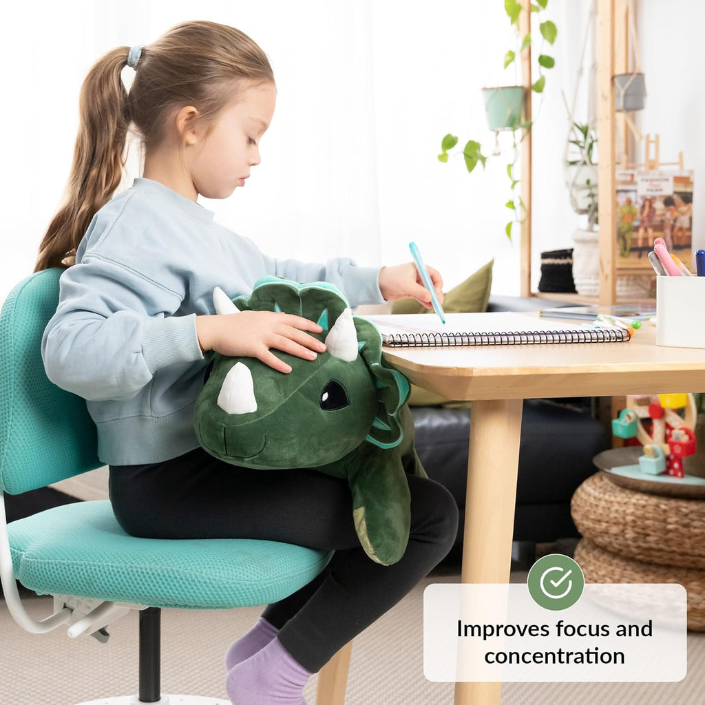 Child sitting on a teal chair with a dinosaur plush toy on her lap, writing in a notebook.