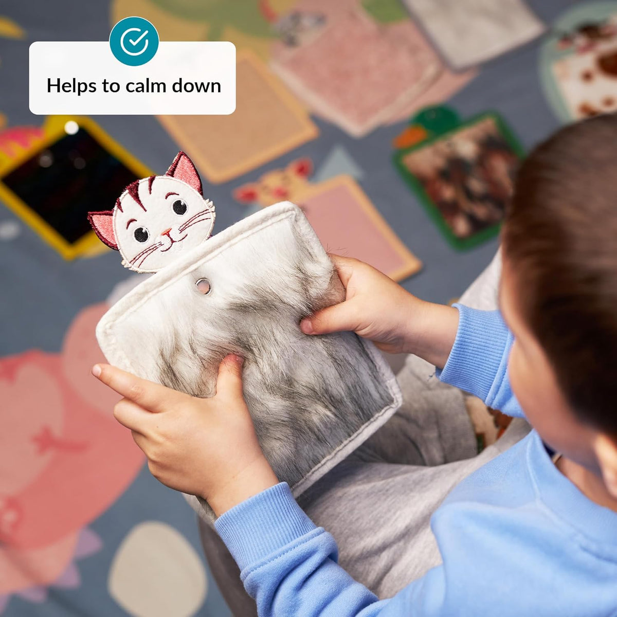Person holding a gray cat-shaped texture mat with a cartoon cat illustration above it.