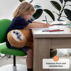 Child sitting at a desk with a sloth-shaped weighted plush toy, surrounded by pencils and books.