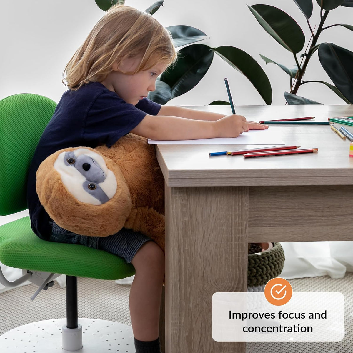 Child sitting at a desk with a sloth-shaped weighted plush toy, surrounded by pencils and books.