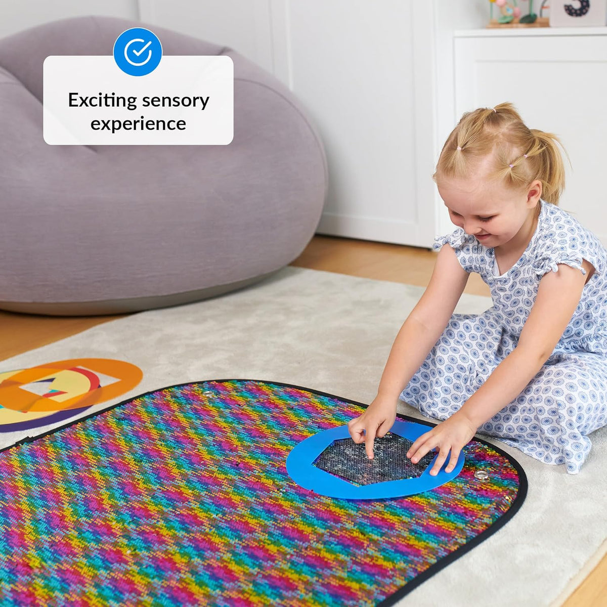 Child playing with a colorful sequins mat on the floor.