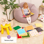 Child sitting on a bean bag touching sensory sheets with educational toys around