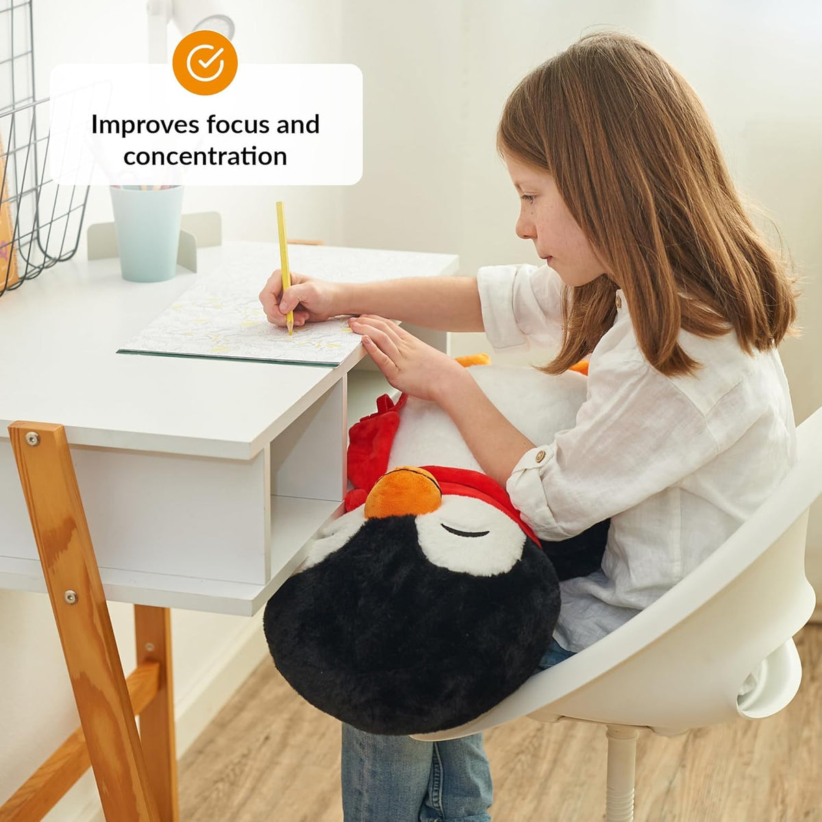 Child sitting at a desk with a penguin weighted plush, improving focus and concentration.