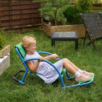 Child sitting in a small green and blue sensory rocking chair on grass