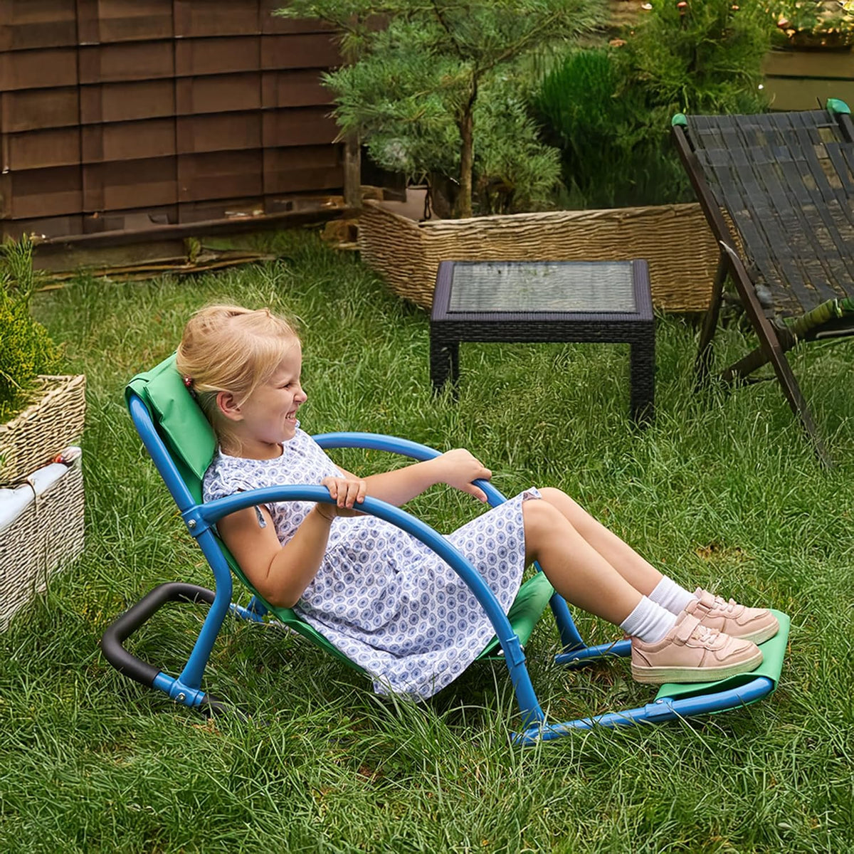 Child sitting in a small green and blue sensory rocking chair on grass
